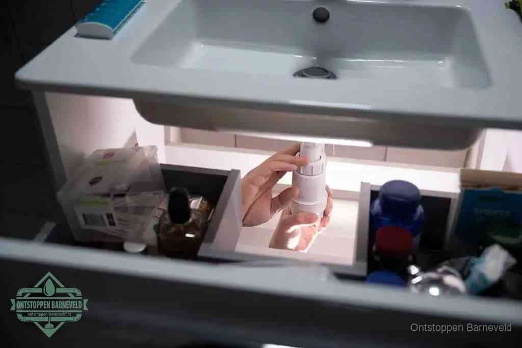 Een pompfles met zeep boven een wastafel, de heet water en afwasmiddel-methode om een vetprop in de afvoer los te maken in Barneveld