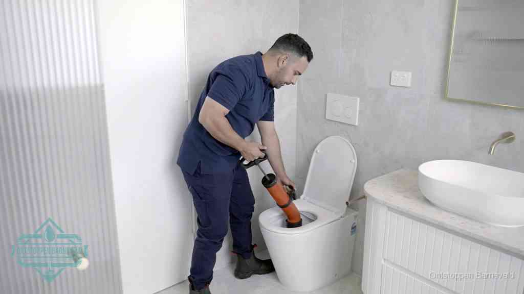 Een monteur buigt over een wandcloset en duwt met de hand een persluchtontstopper in de toiletpot om de verstopping handmatig los te maken in Barneveld