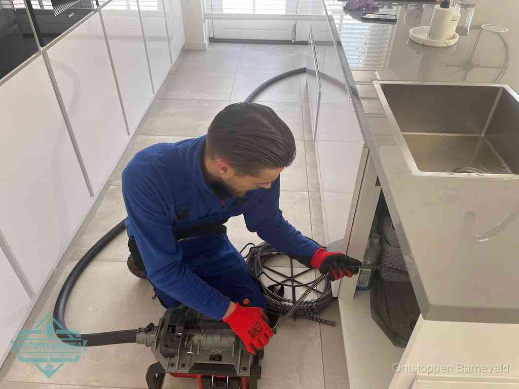 Een monteur ontstopt de keukenafvoer onder de spoelbak met een elektrische veermachine in Barneveld