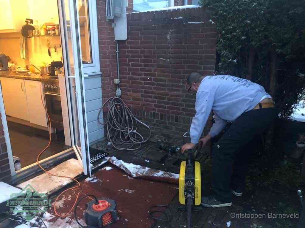 Een monteur werkt buiten bij een open riool-/grondput met een elektrische ontstoppingsmachine om een verborgen afvoerprobleem op te sporen in Barneveld