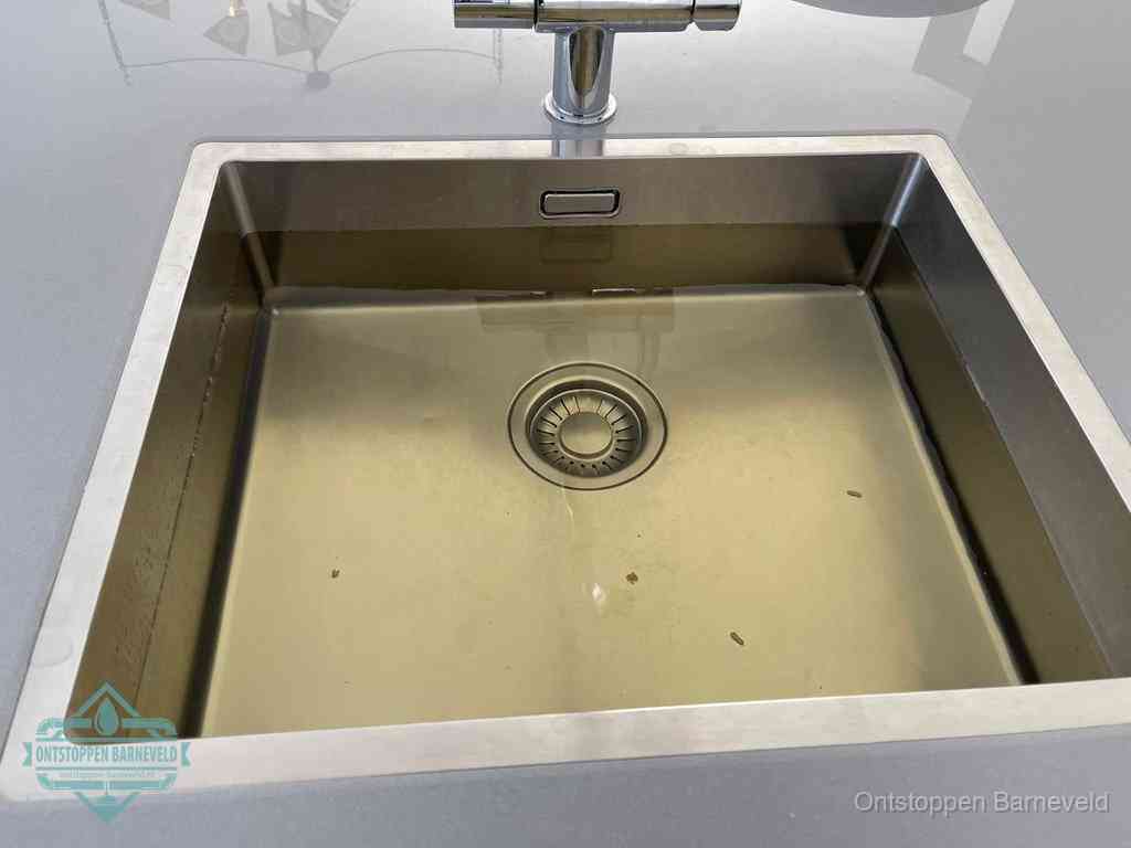 Stilstaand water in een rvs spoelbak dat niet wegloopt, een duidelijk signaal van een gootsteenverstopping in Barneveld