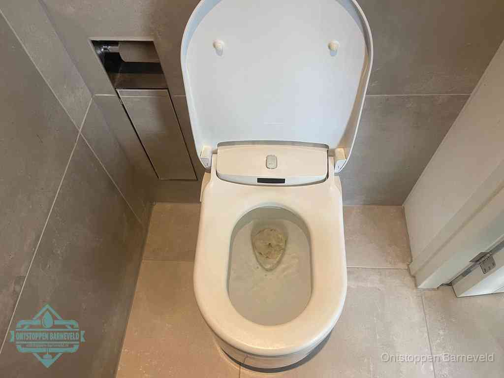 Een wit hangtoilet waarin een prop wc-papier op het water blijft drijven, een duidelijk signaal van een verstopte wc in Barneveld