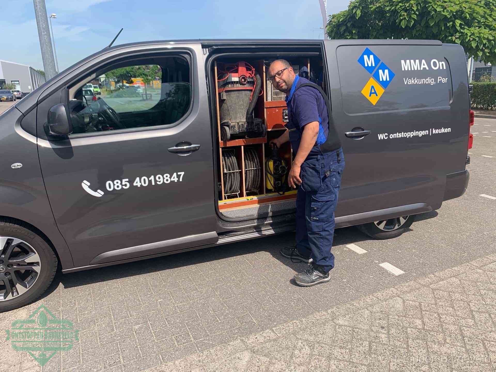 Een monteur bij de open schuifdeur van zijn bedrijfsbus op een parkeerplaats, klaar om de oorzaak van terugkerende afvoerverstoppingen aan te pakken in Barneveld