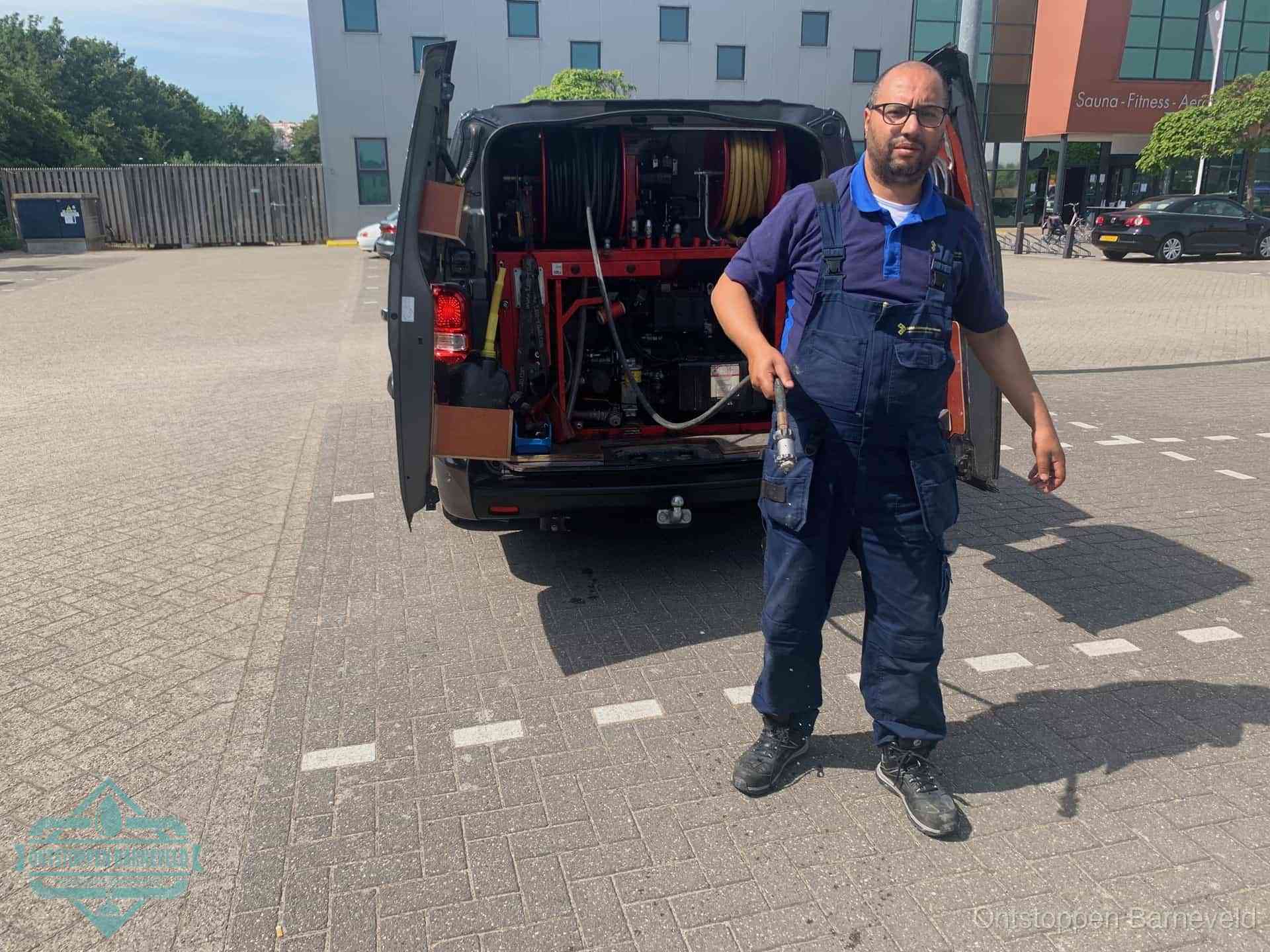 Een monteur bij zijn bestelbus met een hogedruk- en rioolreinigingsunit, klaar om de oorzaak van terugkerende wc-verstoppingen aan te pakken in Barneveld