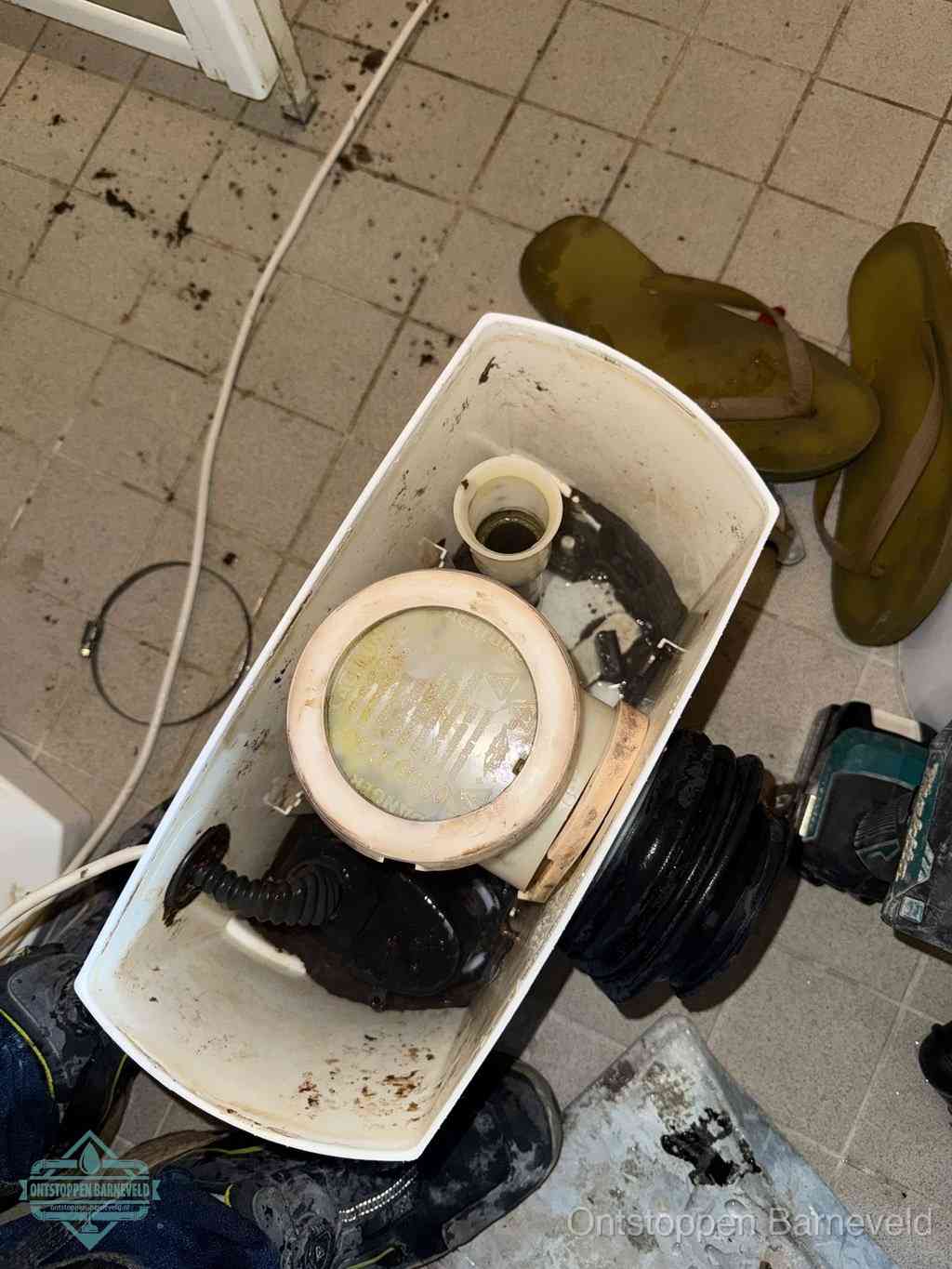 Een gedemonteerde toiletpot op de vloer met ontstoppingsveer en gereedschap ernaast, het verwijderen van een vastzittend voorwerp uit de wc in Barneveld