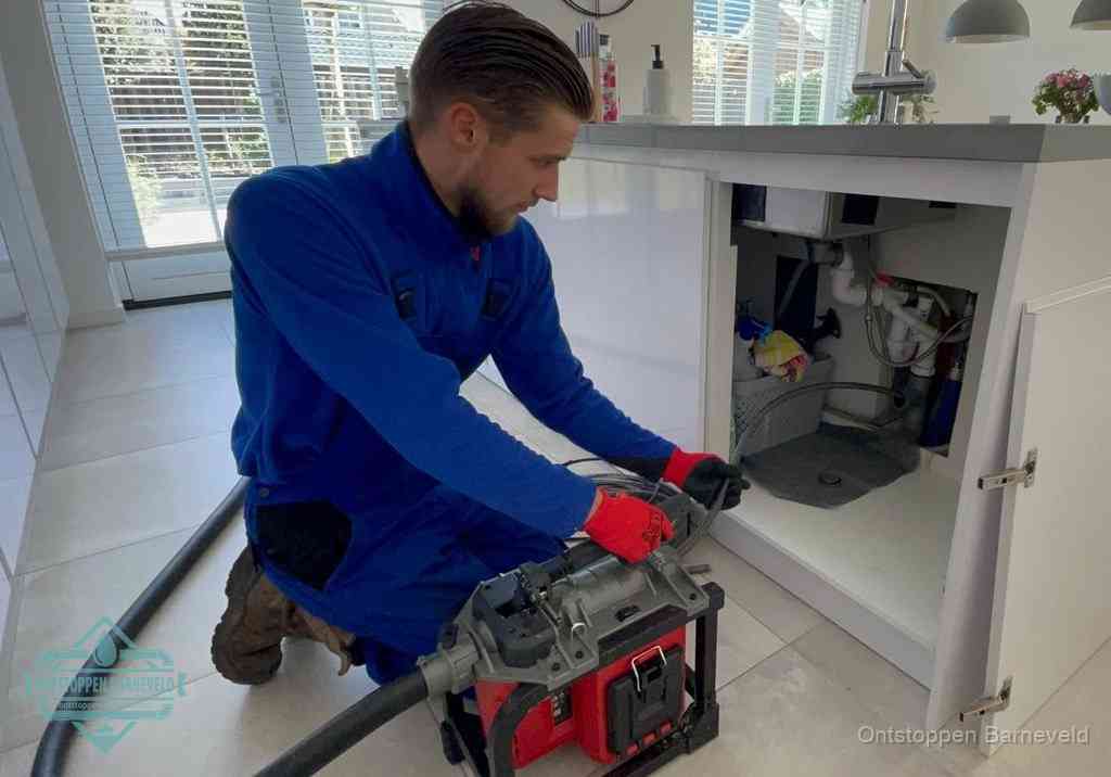 Een monteur voert een professionele elektrische ontstoppingsmachine in de afvoer onder de spoelbak tijdens het gootsteen ontstoppen in Barneveld