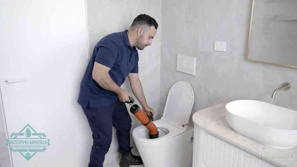 Een monteur gebruikt een handmatige perspomp (toiletontstopper) op een wandcloset tijdens het professioneel wc ontstoppen in Barneveld