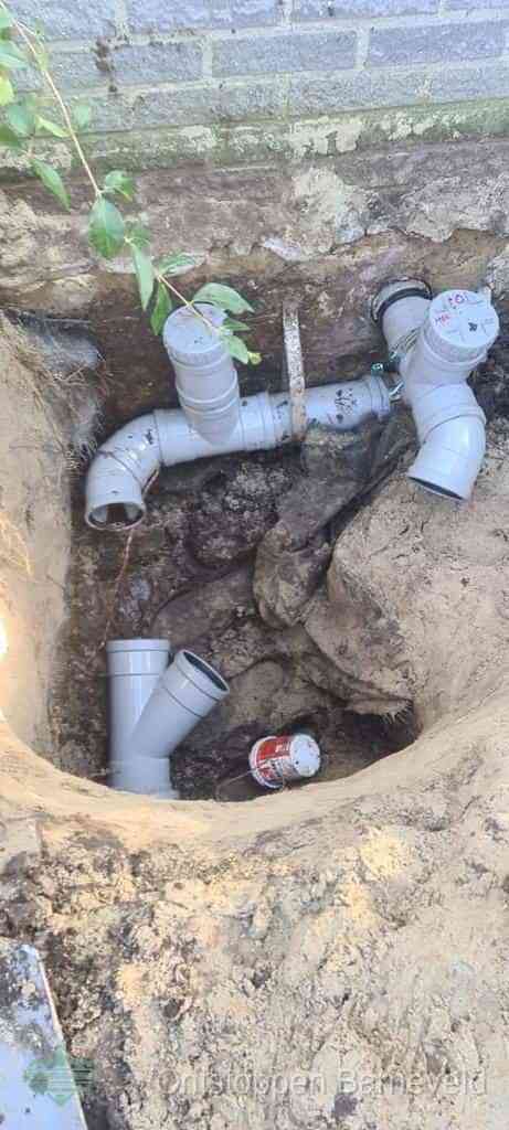Een opgegraven bouwput langs een huismuur met grijze PVC rioolbuizen die op het hoofdriool worden aangesloten, typisch leidingwerk per wijk in Barneveld