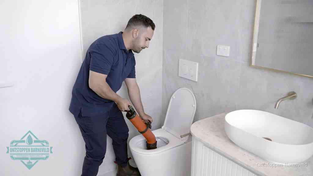 Een man gebruikt een handmatige luchtdruk-ontstopper in een modern betegeld toilet om zelf de wc te ontstoppen in Barneveld